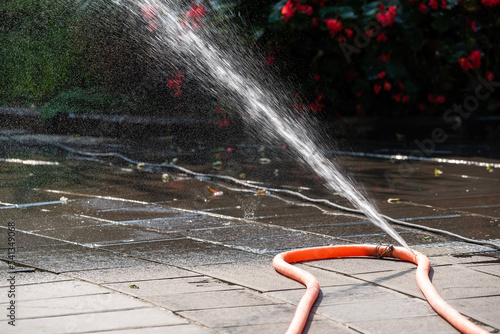 Water flowing from a leaky orange garden hose against sun light photo