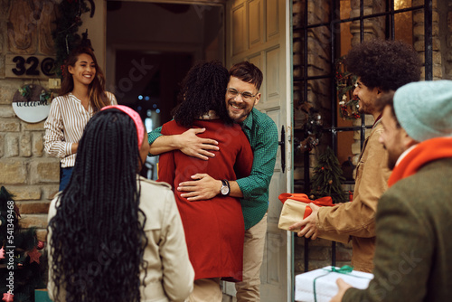 Photography Happy man embracing one of friends while welcoming guests with his wife at the doorstep