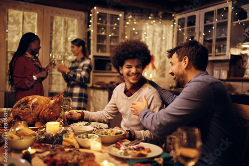 Young happy men talk at dining table during Thanksgiving dinner.