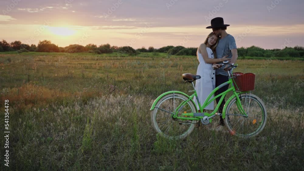Couple watches summer sunset holding handlebar of bicycle Couple watches summer sunset holding handlebar of bicycle