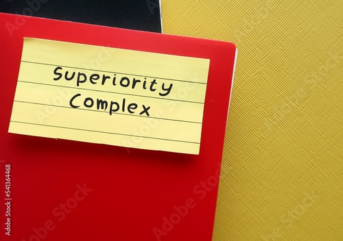 Red notebook on yellow background with handwritten text SUPERIORITY COMPLEX, means belief that your abilities or accomplishments are dramatically better than someone else