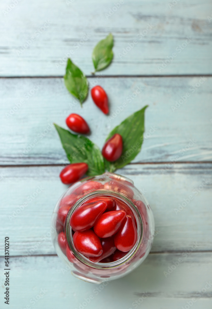 Jar with ripe red dogwood berries and leaves on color wooden background
