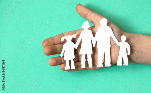 paper cut family in child's hand, green background. child care, guardianship and adoption concept. family violence against children. orphanage