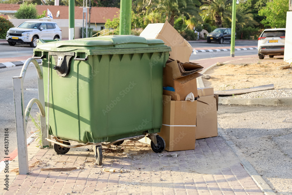 Green garbage container with cardboard on city street Green garbage container with cardboard on city street