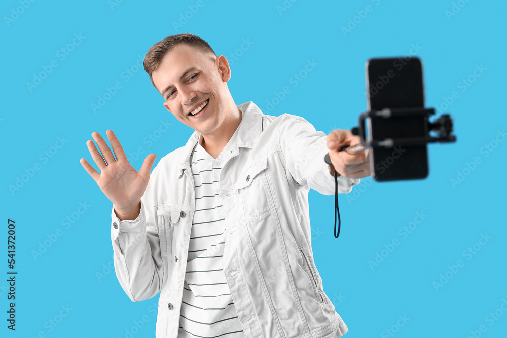Naklejka premium Young man with mobile phone taking selfie on blue background