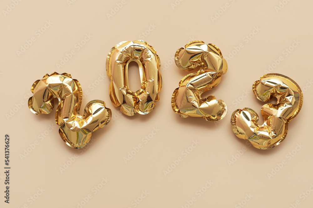 Figure 2023 made of golden balloons on beige background Figure 2023 made of golden balloons on beige background