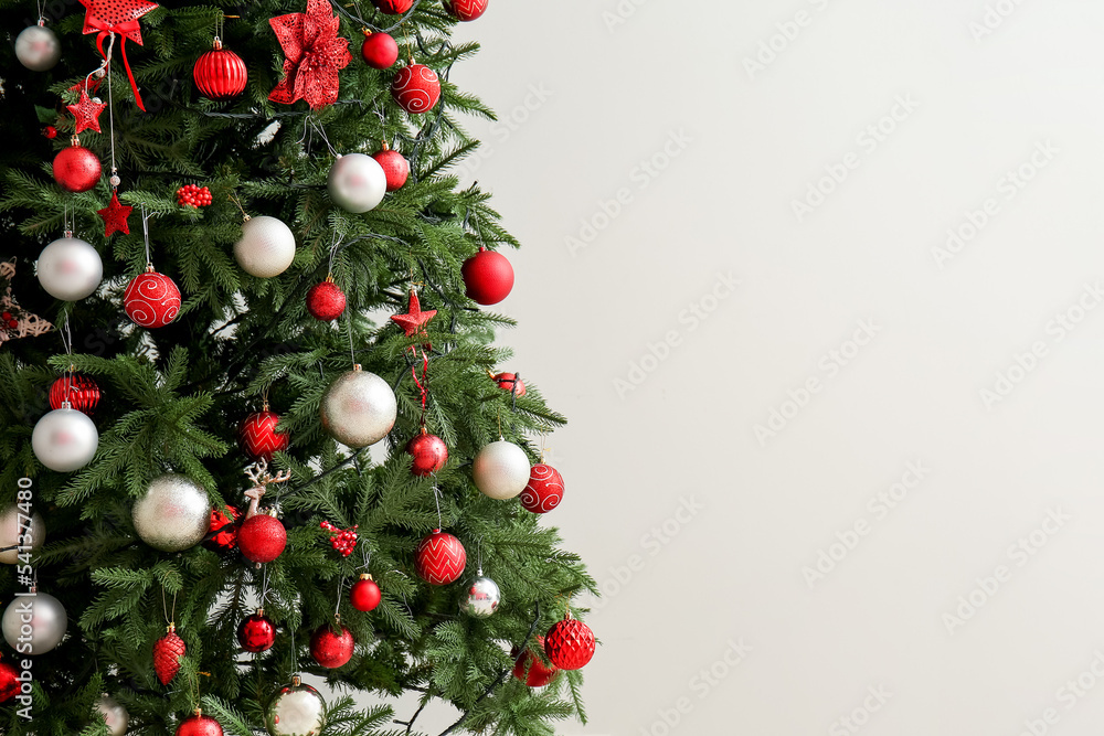 Big Christmas tree with decor near light wall