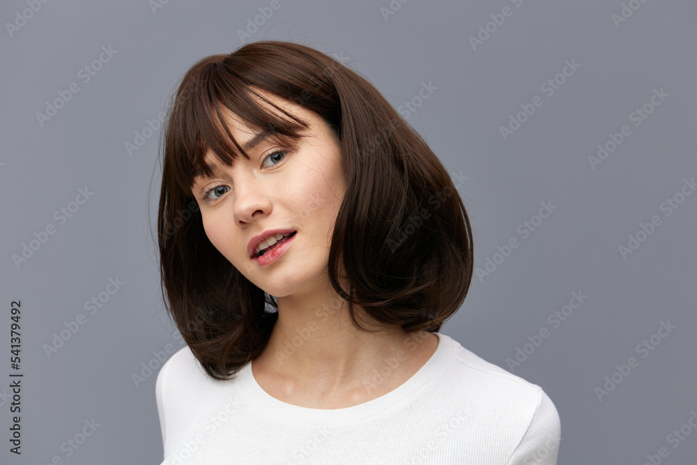 Fototapeta premium a sweet, beautiful, happy woman smiles pleasantly looking at the camera standing on a gray background in a white T-shirt