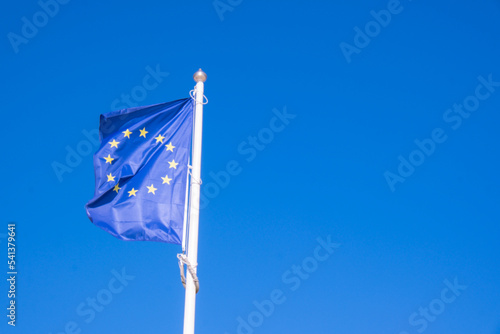 EU European flag poole blowing in the wind on a bright sunny summers day. Frayed European Union flag is fluttered by strong wind, blue sky background.