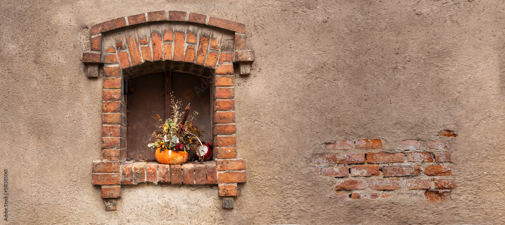 Małe okienko ozdobione bukietem jesiennych kwiatów i dynią w ceglanym budynku - obrazy, fototapety, plakaty 