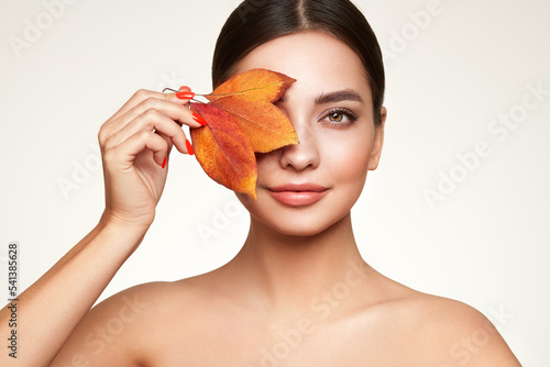 Portrait of beautiful young woman with autumn leafs. Healthy clean fresh skin natural make up beauty eyes and red nails