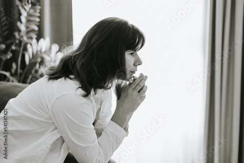 middle-aged woman is sitting on a sofa in a room and is sad, mental health, stress and hypochondria, worries and anxiety, black and white photo