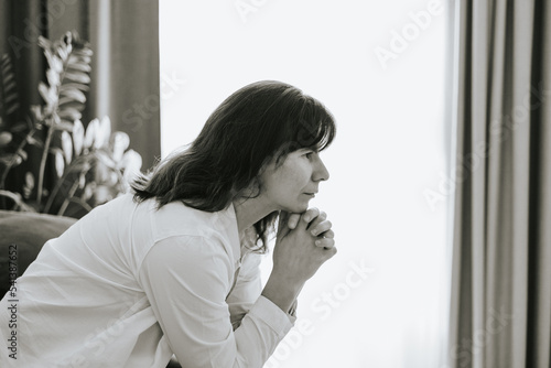 middle-aged woman is sitting on a sofa in a room and is sad, mental health, stress and hypochondria, worries and anxiety, black and white photo