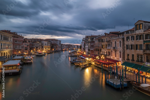 Evening over the Grand Canal from Rialto Bridge in Venice, Italy. The sky is cloudy and the canal is lit up