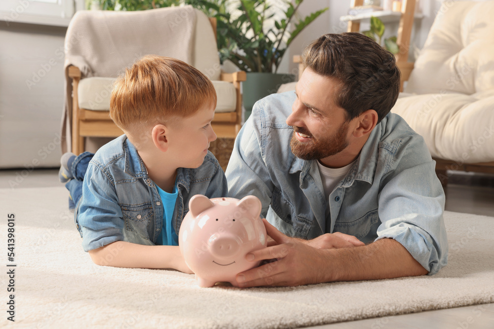 Father and his son with ceramic piggy bank on floor at home Father and his son with ceramic piggy bank on floor at home