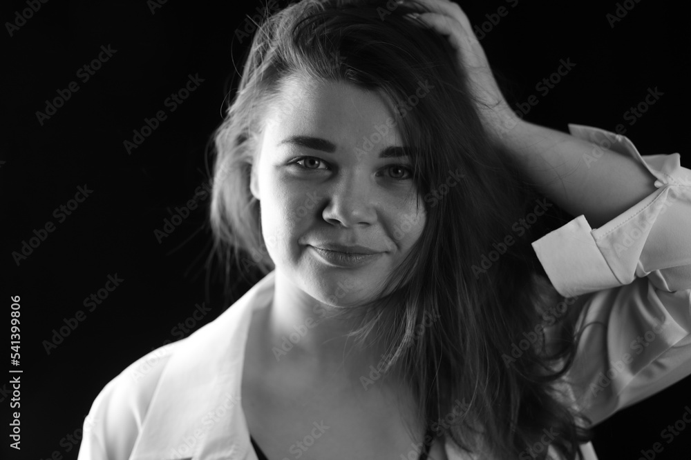 Beautiful girl straightens her hair, portrait on a black background, black and white photo Beautiful girl straightens her hair, portrait on a black background, black and white photo