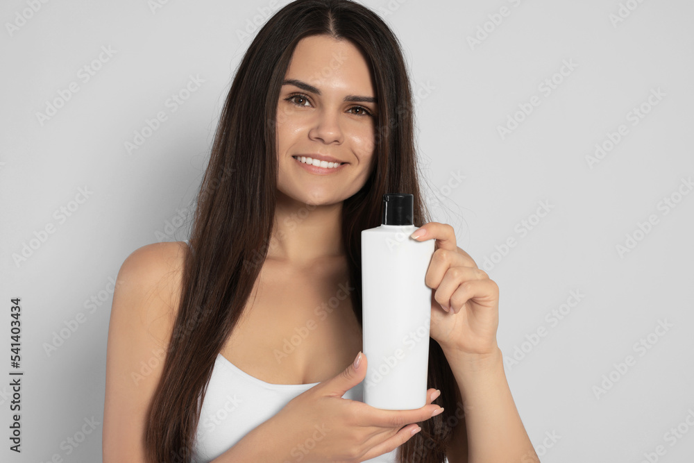 Beautiful young woman holding bottle of shampoo on white background Beautiful young woman holding bottle of shampoo on white background