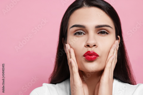 Beautiful young woman giving kiss on pink background, closeup