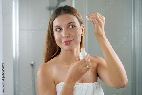 Portrait of a young woman applying Retinol on her face at home. Skin care routine. photo