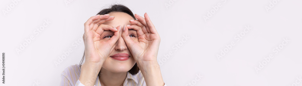 Close up portrait of attractive quirky young woman making binoculars with hands showing ok gesture on white studio background.