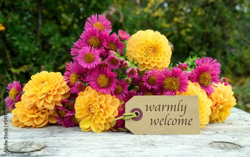 Greeting card with a bouquet of autumn flowers and the text in English: warmly welcome