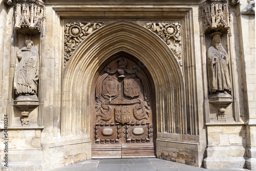 Entrance with decorated wooden door of famous Abbey Church of Saint Peter and Saint Paul at City of Bath on a blue cloudy summer day. Photo taken August 2nd, 2022, Bath, United Kingdom.