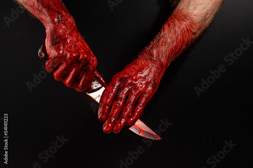 A man wipes a bloody knife with his hand on a black background. 