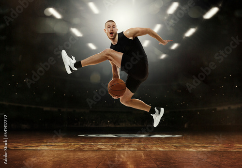 Energetic young professional basketball player jumping with ball at basketball court with people fans. Photoreal 3d render of sport arena.