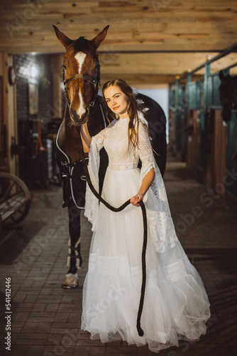 A boho bride poses with a horse in a stable.