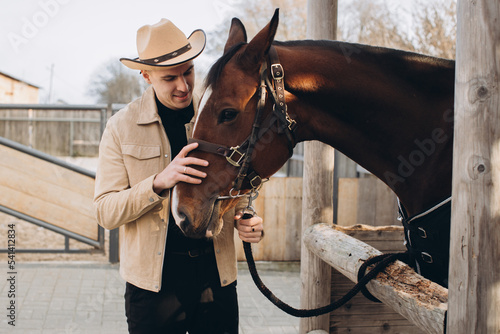 Handsome young cowboy on a ranch with a horse.