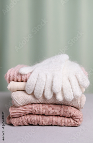 Warm woolen gloves of white color are lying on a stack of knitted things. Vertical photo.