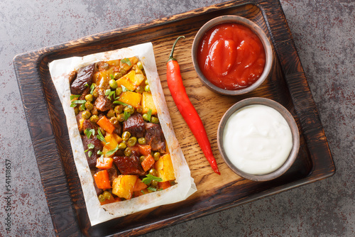 Turkish kebab with potatoes, green peas, onions and carrots wrapped in paper and baked close-up on a wooden tray on the table. Horizontal top view from above photo