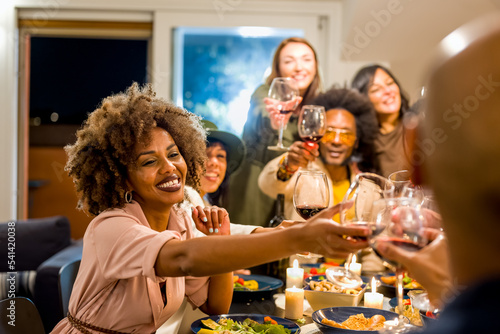 Mixed age range group of friends toasting at dinner party, focus on woman face, Brazilian people drinking red wine and eating vegan food, happy family cheering and toasting