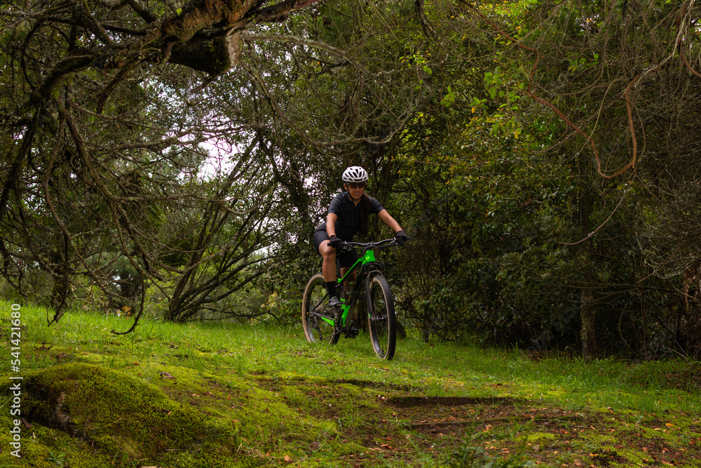 Cyclist woman with helmet and goggles riding her bike in the middle of a forest Cyclist woman with helmet and goggles riding her bike in the middle of a forest