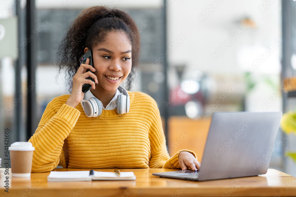 Portrait of an African businesswoman smiling cheerfully and talking on the phone with a colleague about the report. Income from the online business on the laptop at her desk. Portrait of an African businesswoman smiling cheerfully and talking on the phone with a colleague about the report. Income from the online business on the laptop at her desk.