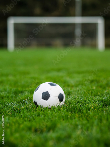 Classic soccer of football ball on the dark green grass field in focus. Goal post out of focus in the background. World wide popular sport activity.