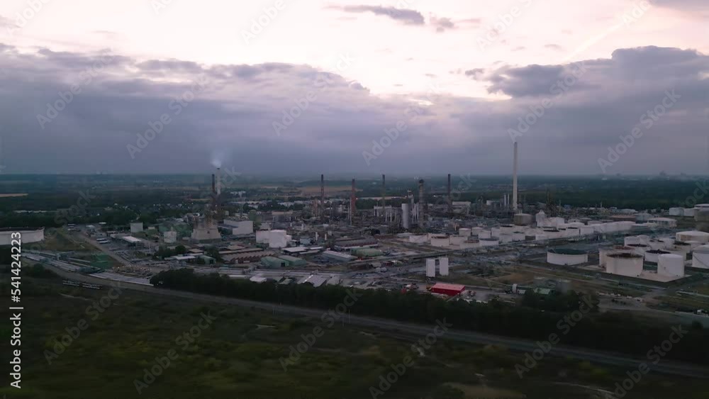 Aerial drone view of chemical oil gas plant company in front of an dark cloudy sky - establishing bird view eshot with an tiny tram crossing the scene in the foreground - big smoking chimneys Aerial drone view of chemical oil gas plant company in front of an dark cloudy sky - establishing bird view eshot with an tiny tram crossing the scene in the foreground - big smoking chimneys