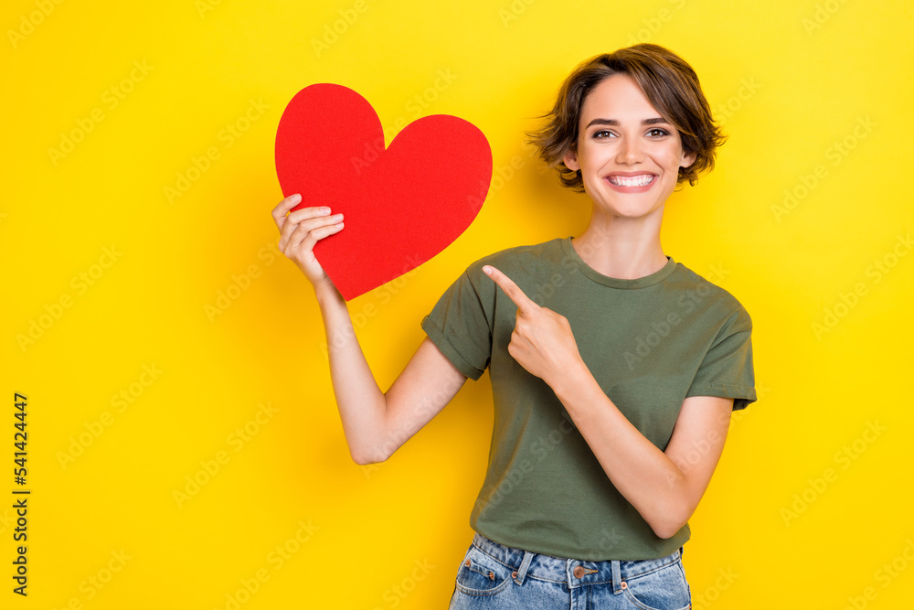 Photo of lovely toothy beaming woman bob hairdo dressed khaki t-shirt directing at big paper red like isolated on yellow color background Photo of lovely toothy beaming woman bob hairdo dressed khaki t-shirt directing at big paper red like isolated on yellow color background