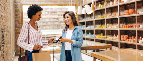 Happy shop owner receiving a contactless credit card payment from a customer photo