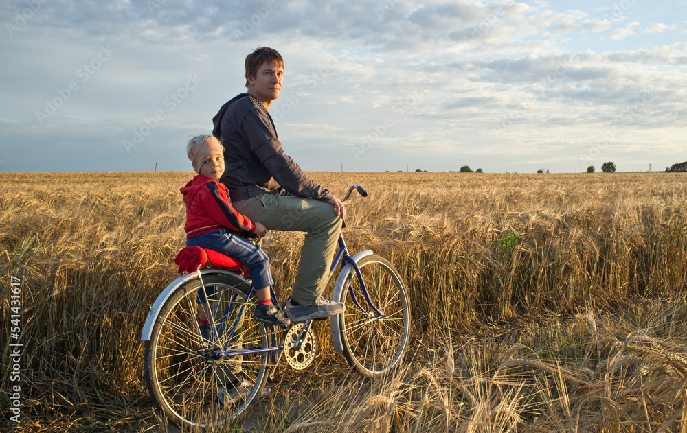 Father with his son on the bicycle trip in the fields. Full-length portrait of the men with small boy on the bicycle