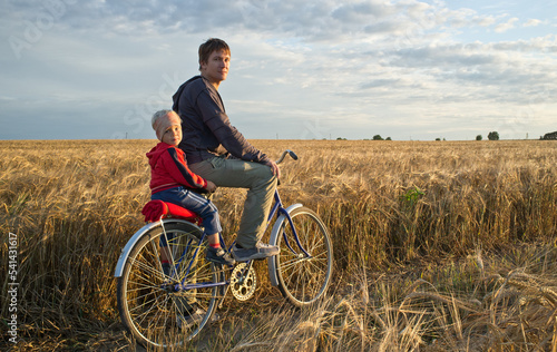 Father with his son on the bicycle trip in the fields. Full-length portrait of the men with small boy on the bicycle