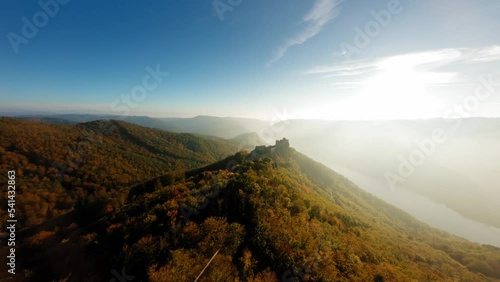 Dynamic ascending shot of wachauer hills, revealing medieval Aggstein covered in evening lights. photo