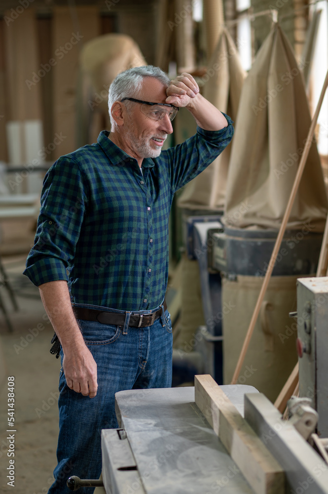 Mature carpenter working in a workshop and looking tired Mature carpenter working in a workshop and looking tired