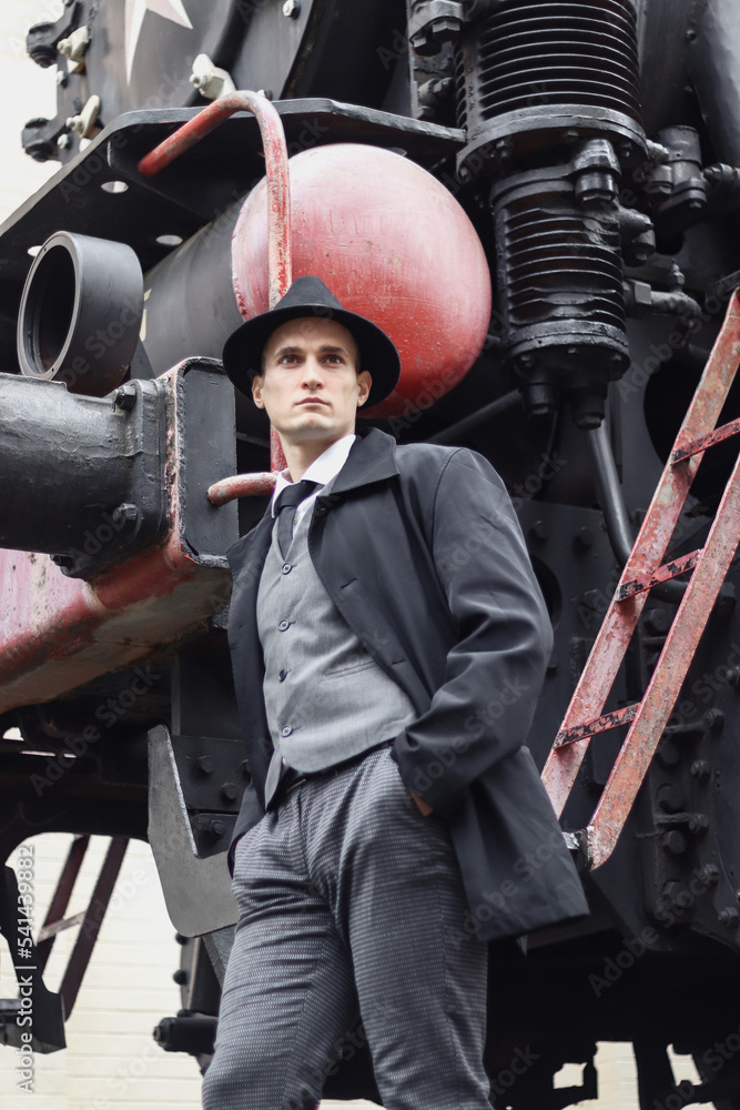 Men's photo session in a classic plaid suit and hat against the backdrop of an old steam locomotive.