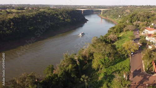 Tourist boat sailing along Iguazu river at border between Argentina and Brazil at sunset with Tancredo Neves bridge in background. Aerial forward photo