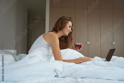 Woman is working after waking up in bed with laptop