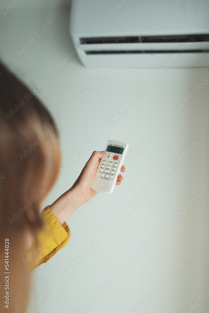 Teenage girl holding remote control aimed at the air conditioner. Teenage girl holding remote control aimed at the air conditioner.