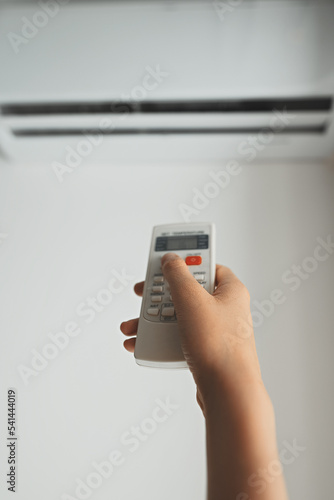 Teenage girl holding remote control aimed at the air conditioner.