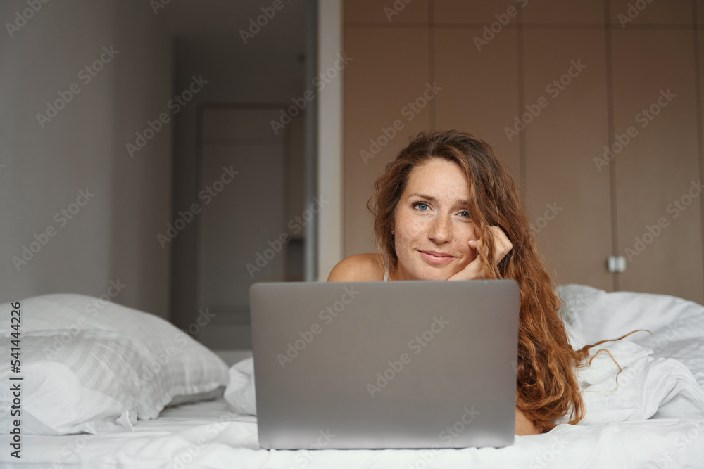 Woman lies on bed with white linens and uses gadget Woman lies on bed with white linens and uses gadget