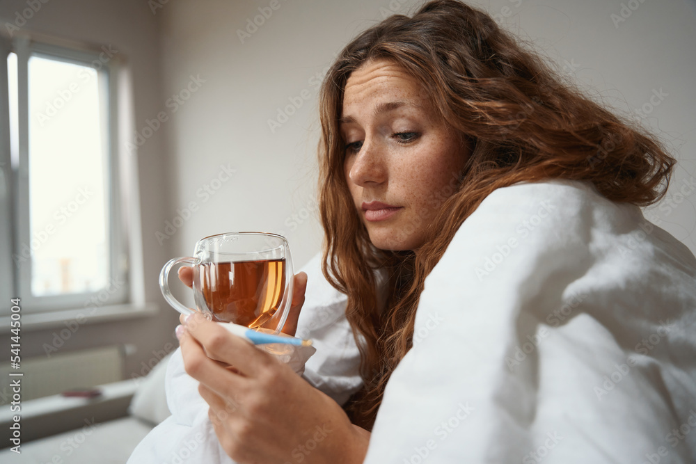 Woman holding an electric body thermometer and cup of tea Woman holding an electric body thermometer and cup of tea